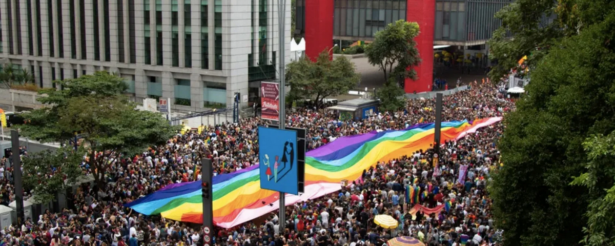 Multidão segurando a bandeira do movimento LGBTQIA+ na Avenida Paulista. Esse é um dos eventos anuais na cidade. 